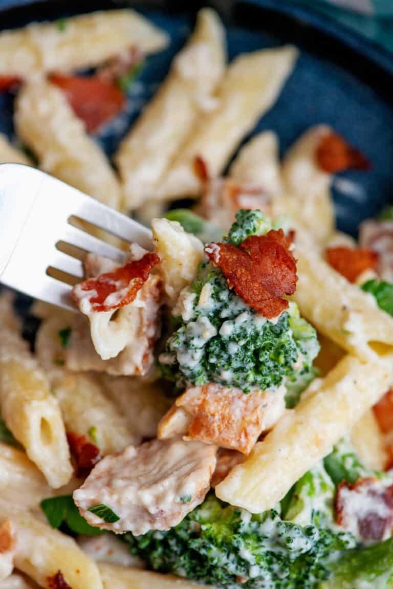 Close-up of a fork digging into chicken bacon ranch penne pasta with broccoli.