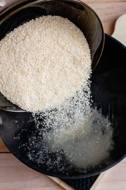 Pouring raw grits into a pot of boiling water.