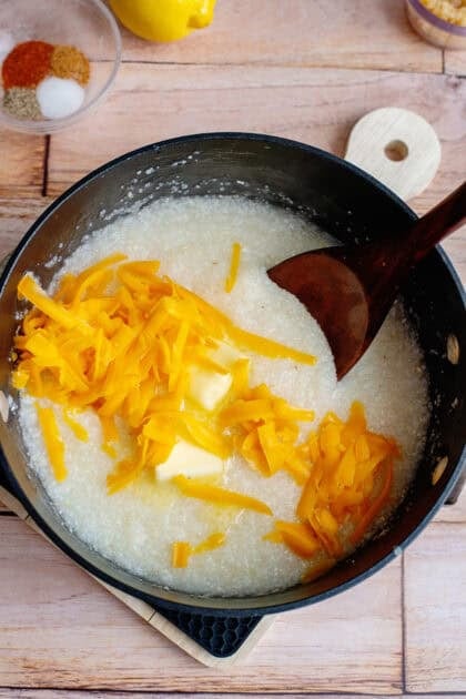 Adding shredded cheddar cheese to a pot of creamy grits.