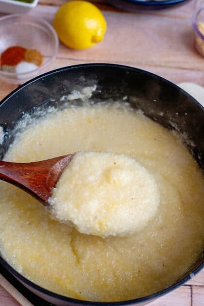 A pot of creamy stone-ground grits simmering on the stove, stirred slowly with a wooden spoon for a smooth texture.
