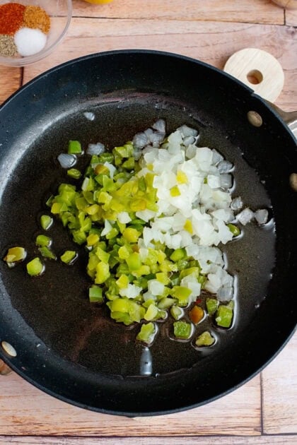 Adding onion and green bell pepper to a skillet.