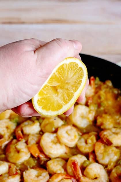 Squeezing lemon juice over shrimp and grits in a pan.