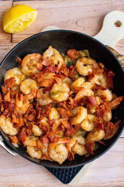 Juicy shrimp cooking in a skillet with butter, garlic, and bacon, turning pink and aromatic.