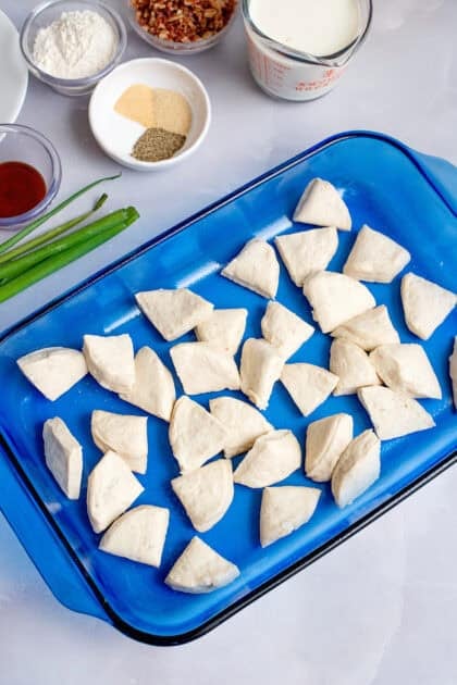 Flaky biscuit dough pieces scattered in a baking dish before being topped with sausage gravy.