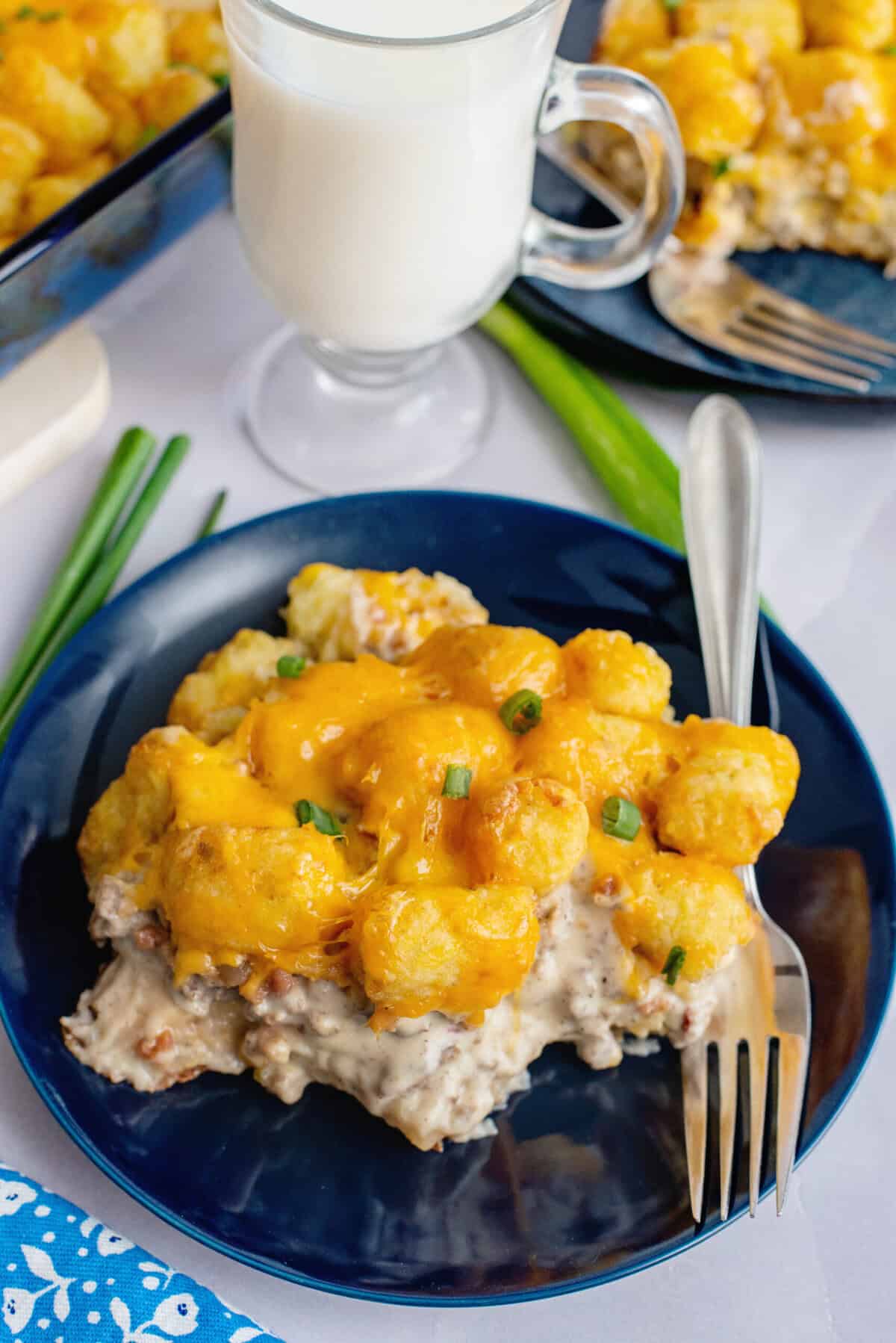A serving of biscuits and gravy tater tot casserole on a black plate with a fork.