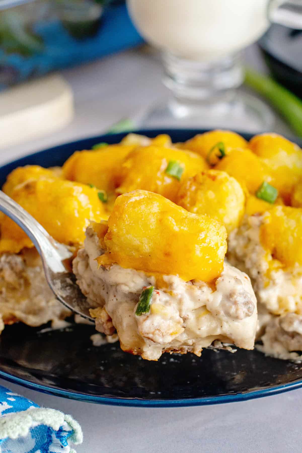 A scoop of hot biscuits and gravy tater tot casserole plated with a sprinkle of fresh parsley for garnish.