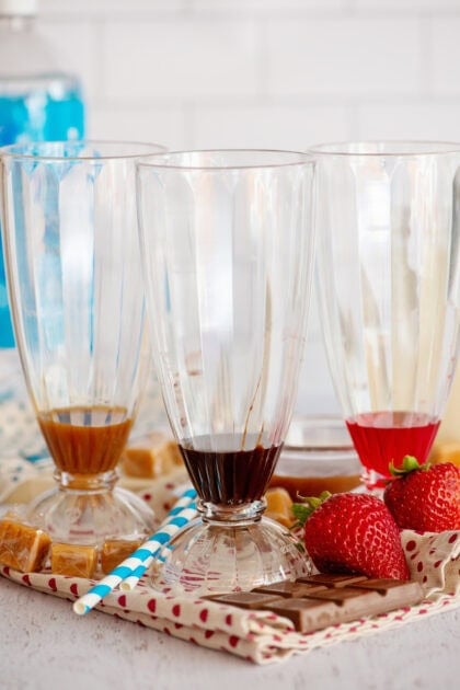 Caramel, chocolate, and strawberry syrup in 3 decorative glasses.