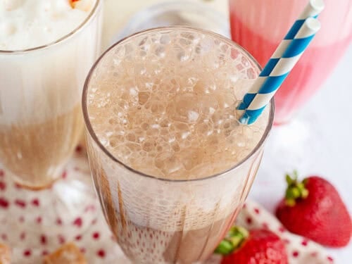 Caramel, chocolate, and strawberry egg creams in decorative glasses with straws.