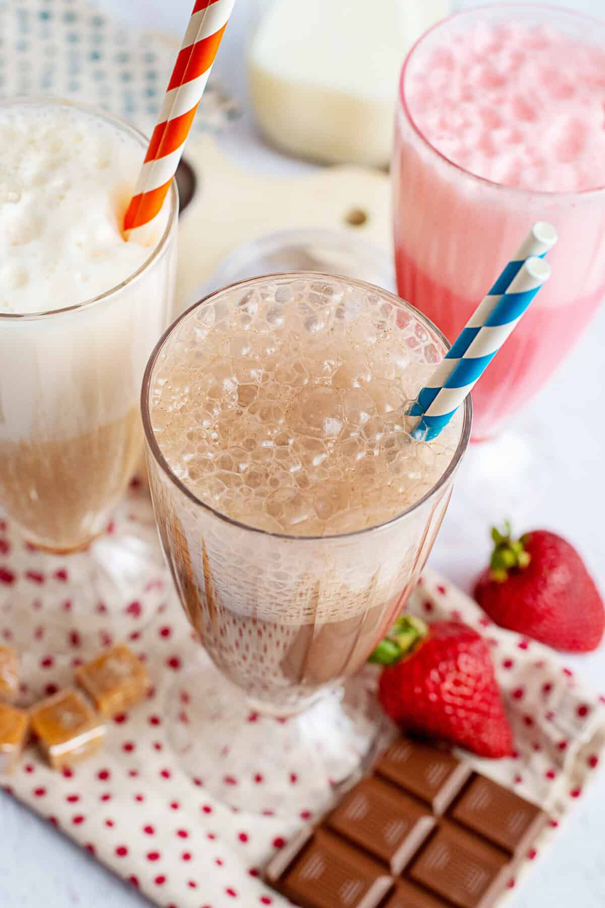 Caramel, chocolate, and strawberry egg creams in decorative glasses with straws.