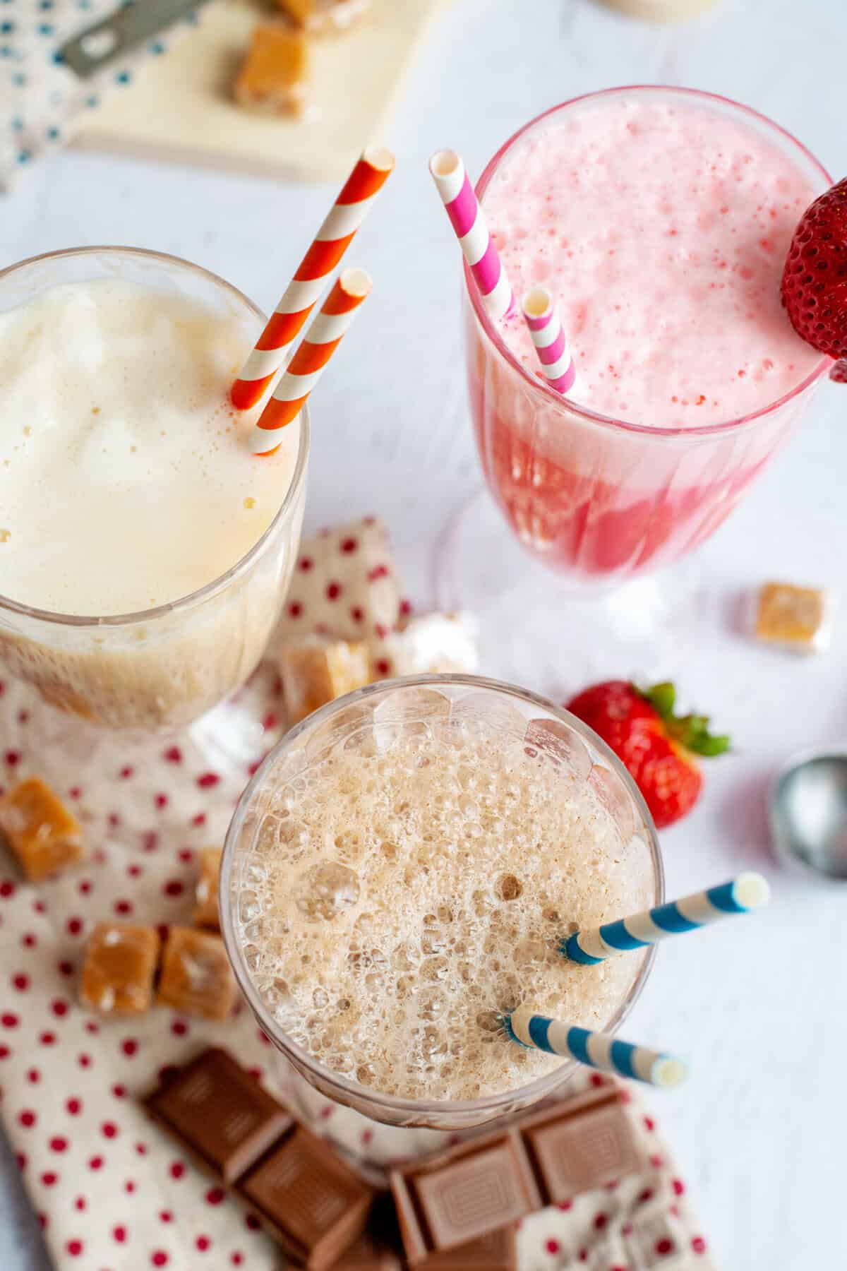 Caramel, chocolate, and strawberry egg creams in decorative glasses with straws.