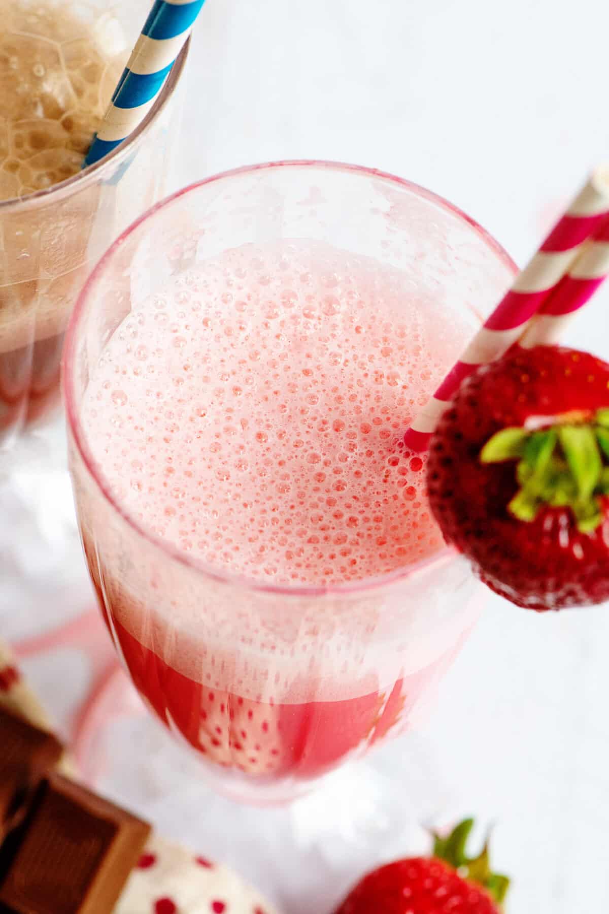 A strawberry egg cream with a straw and strawberry on top.
