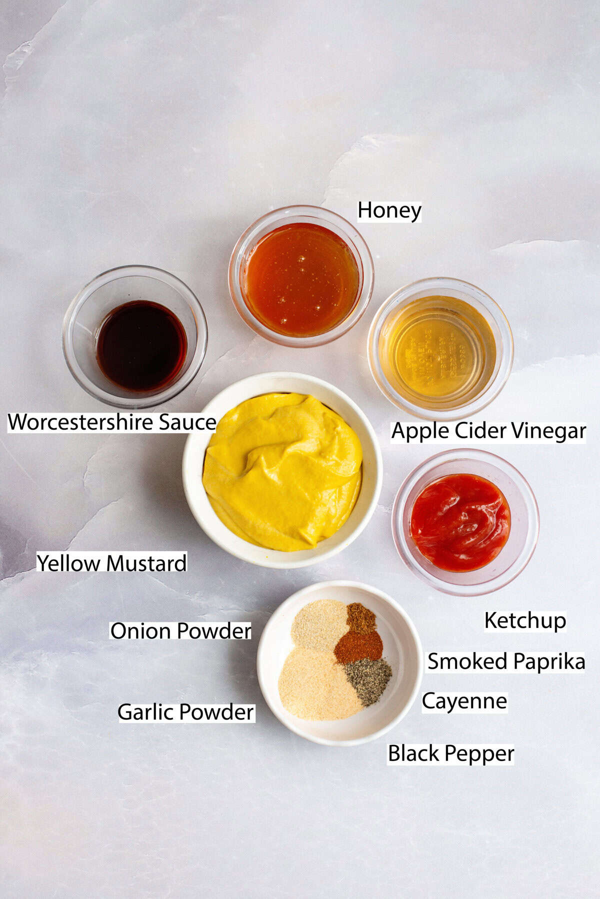 A styled flat-lay of homemade BB Q sauce ingredients on a marble counter with labels.