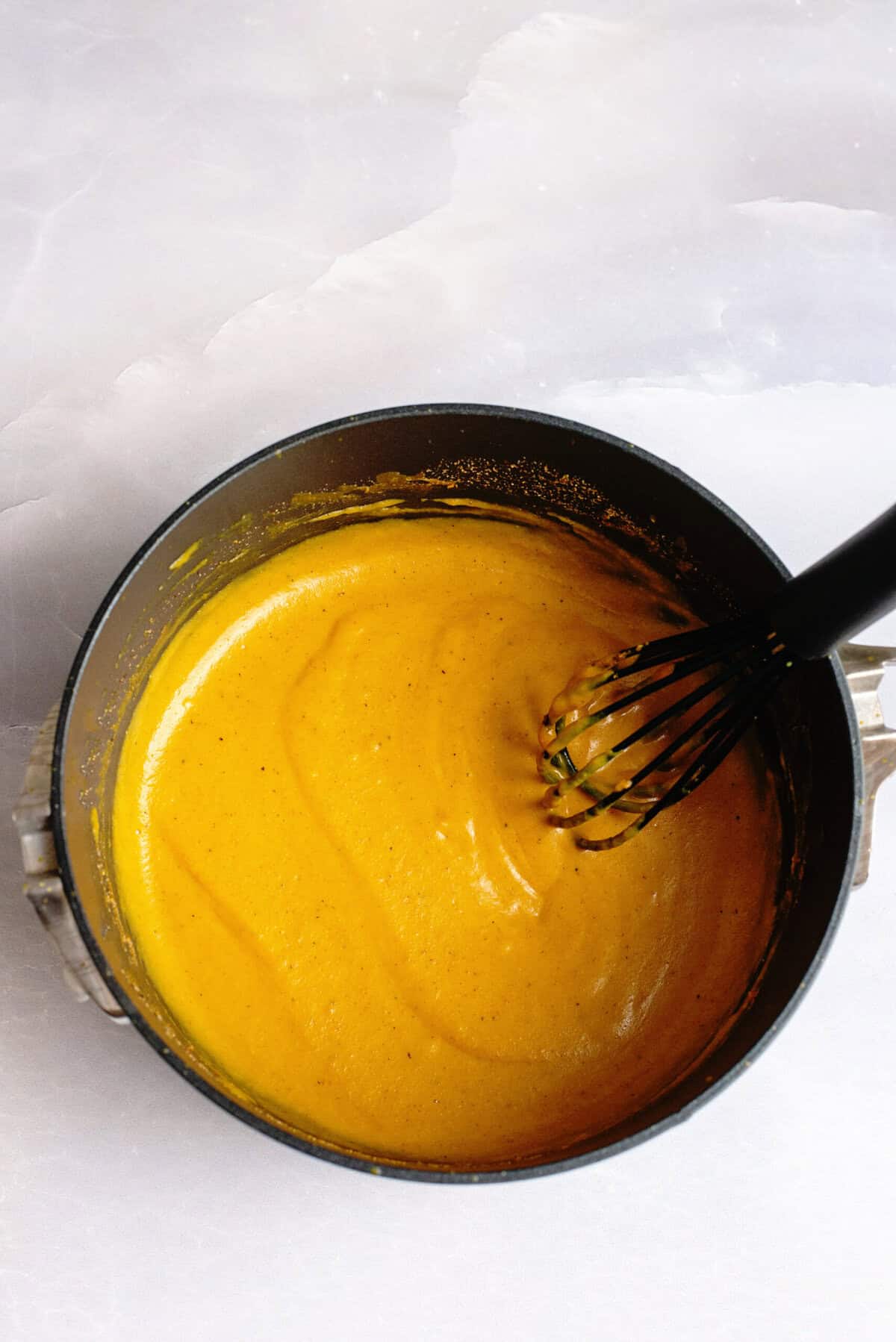 Golden BBQ sauce in a saucepan mid-preparation, a whisk swirling through the thick, glossy mixture with visible spices.