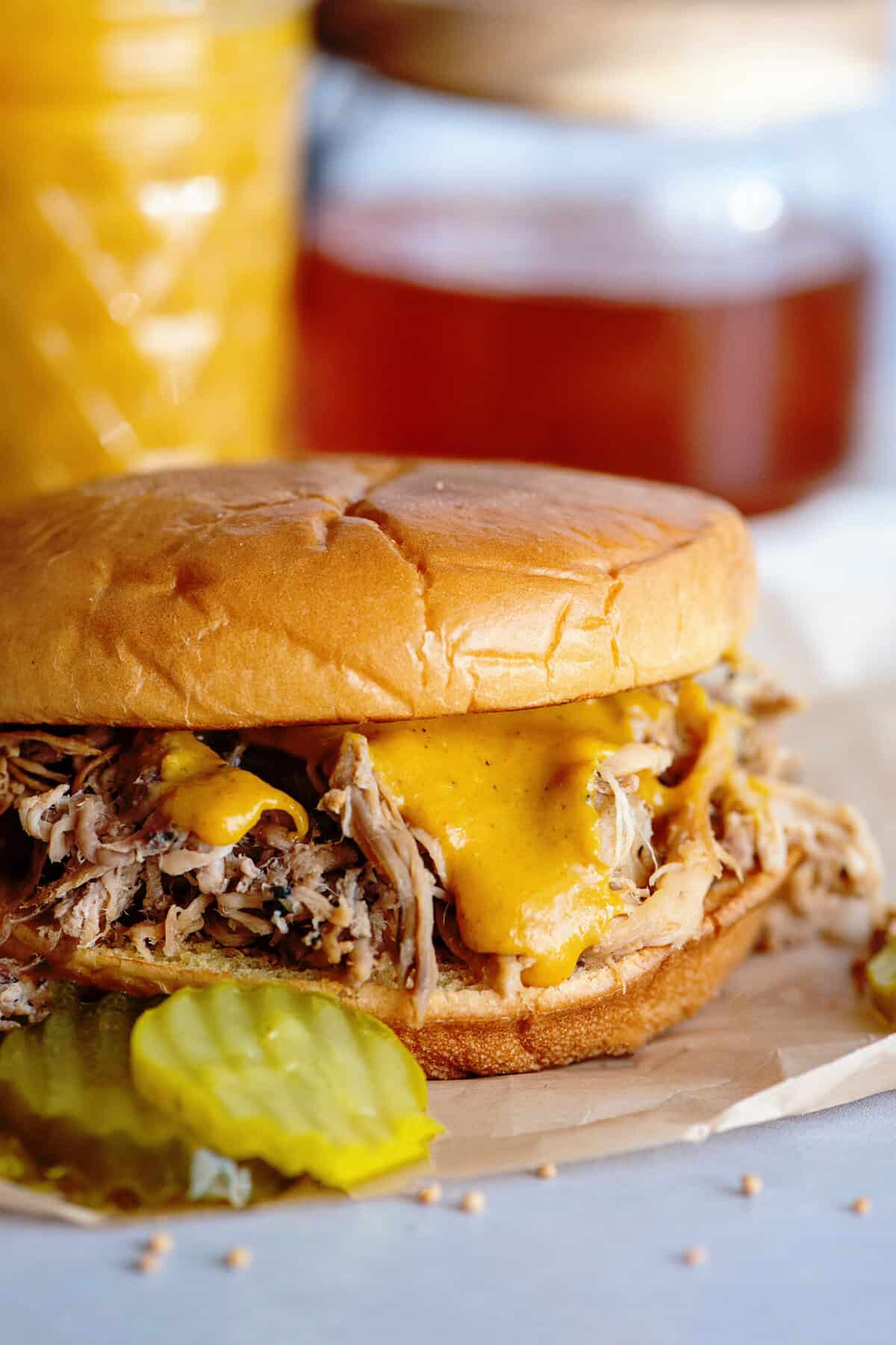 A messy, mouthwatering pulled pork sandwich with Carolina Gold BBQ sauce, open-faced to show the saucy meat, alongside fresh pickles on a rustic plate.