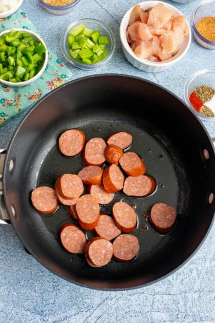 Sliced andouille sausage cooking in a skillet.