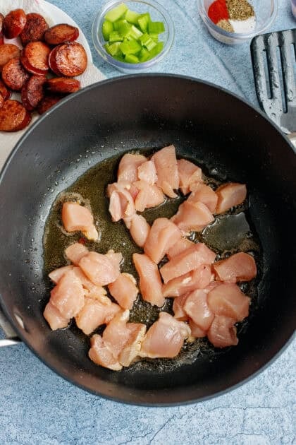 Chicken pieces browning in a cast iron pan.