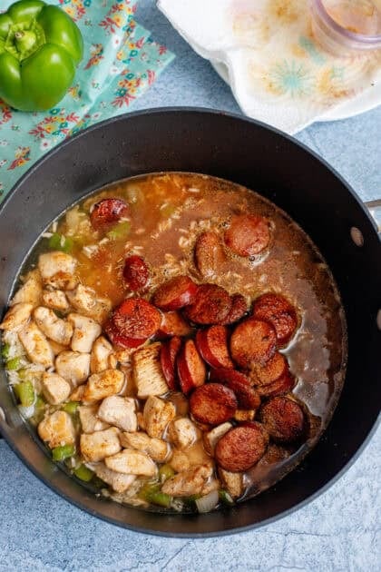 Pouring rich broth into the skillet with meat and veggies.