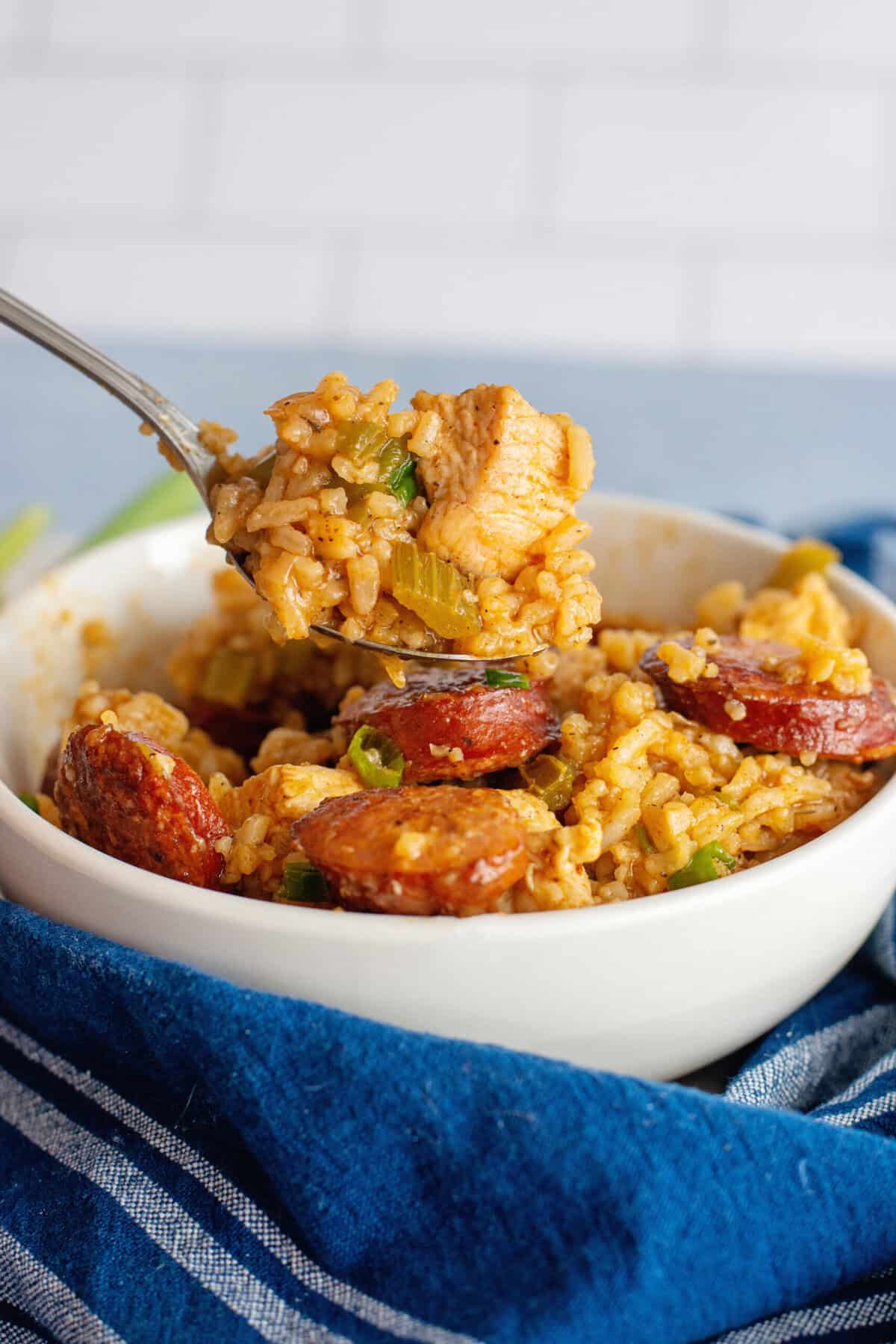 Close-up of a fork lifting juicy chicken and sausage from a bowl of Cajun jambalaya.