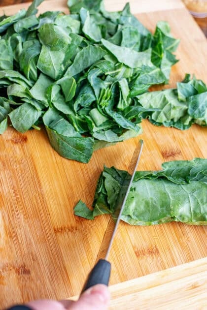 Chopping collard greens on a wooden cutting board.