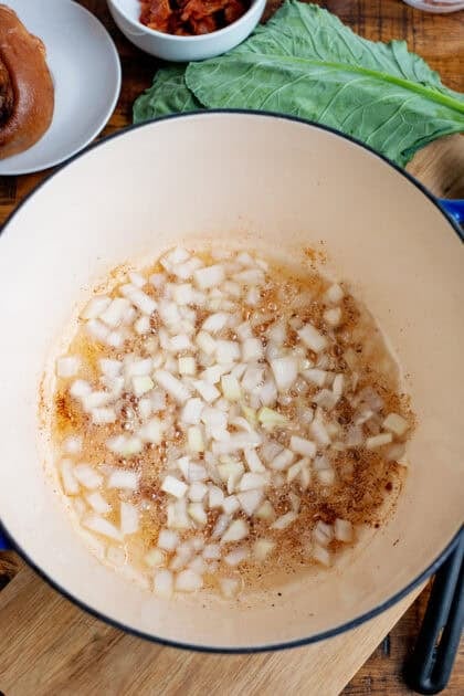 Onions cooking in bacon grease in a Dutch oven.