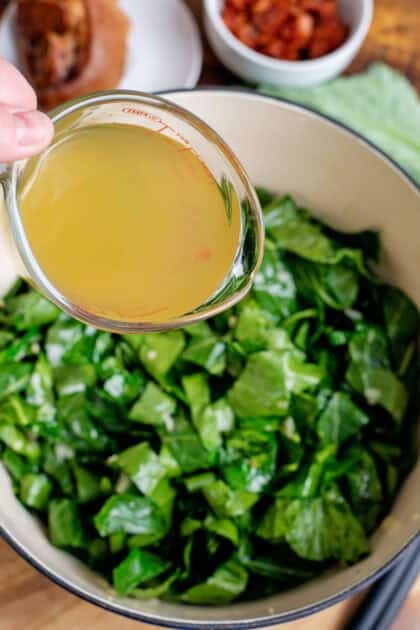 Adding chicken broth to collard greens in a Dutch oven.