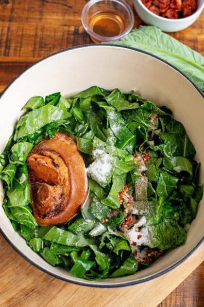 Fresh collard greens in a Dutch oven with a ham hock and baking soda.