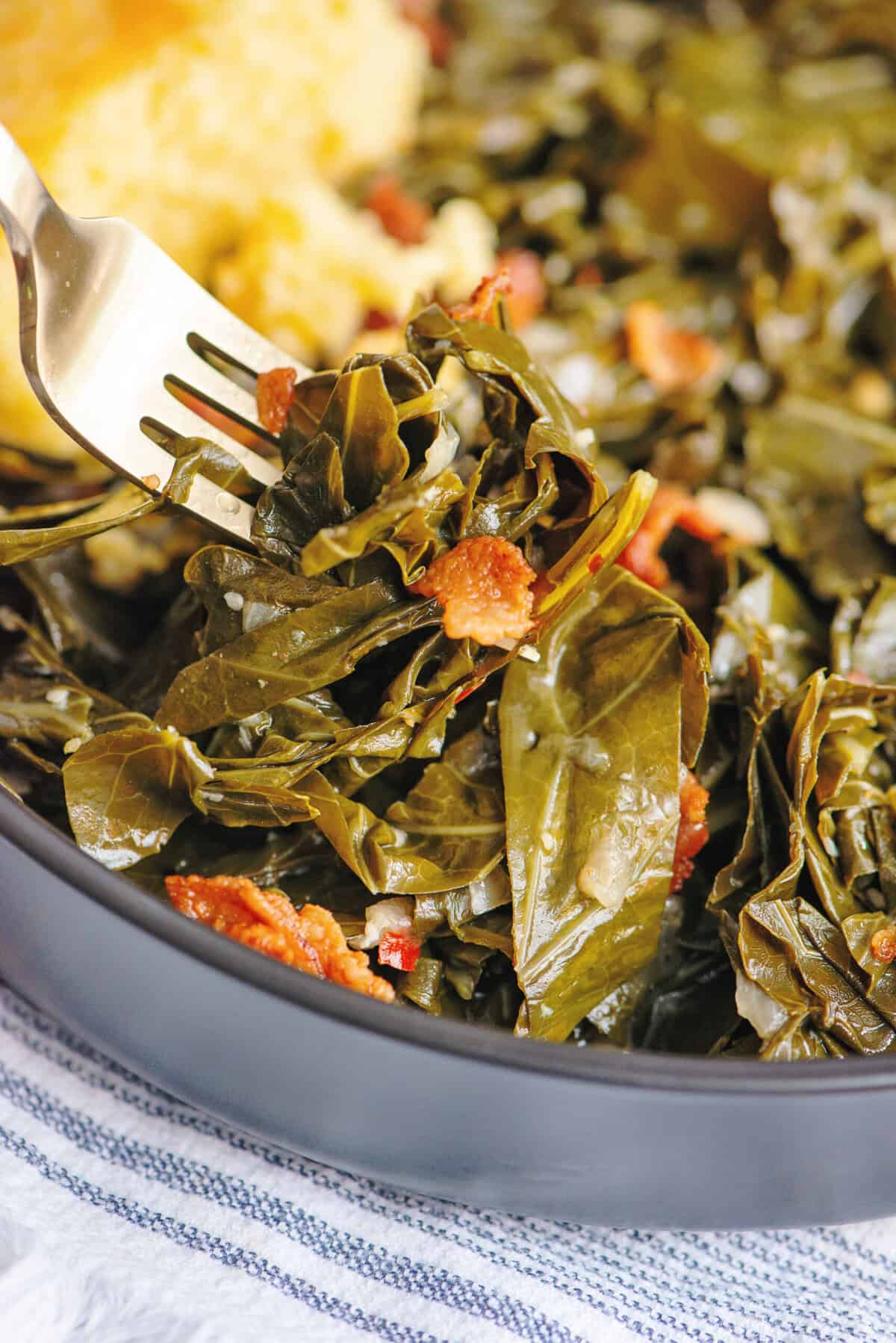 A forkful of collard greens hovering over a black bowl.
