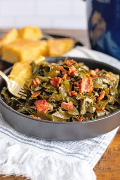 A bowl of collard greens in a black bowl with bacon and cornbread.
