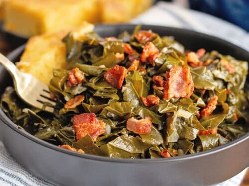 A bowl of collard greens in a black bowl with bacon and cornbread.