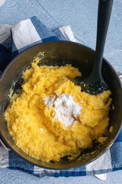 Adding sugar to Southern spoonbread batter in a black mixing bowl.