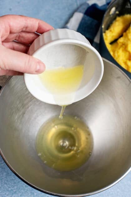 Mixing egg whites with melted butter in a silver mixing bowl.