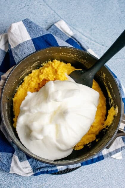 Adding egg white mixture to Southern spoonbread in a black mixing bowl.