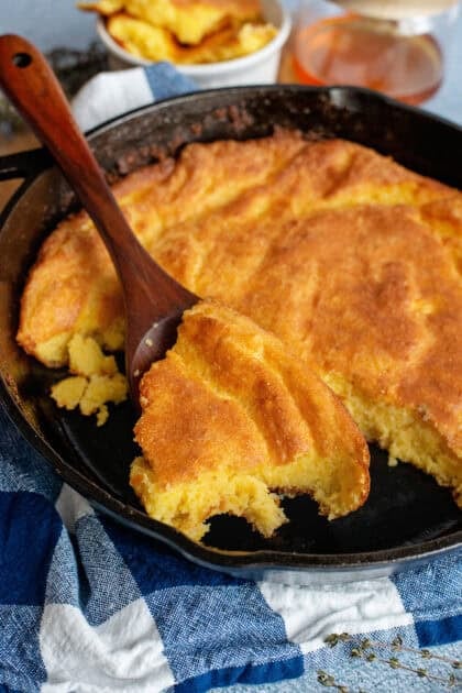 A spoon scooping Southern spoonbread from a cast-iron skillet.