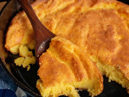 A spoon scooping Southern spoonbread from a cast-iron skillet.