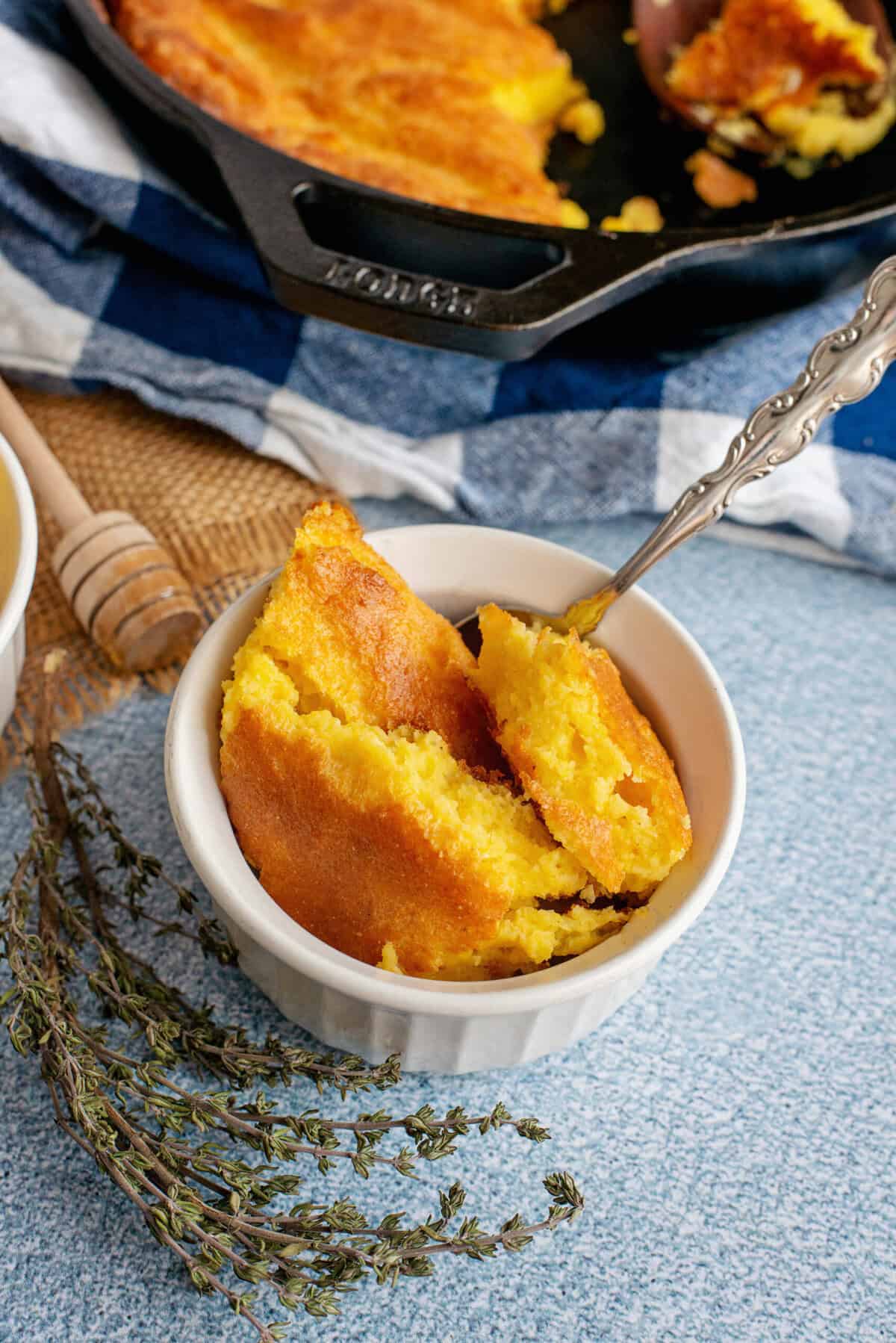 Southern spoonbread in a white baking dish drizzled with honey.