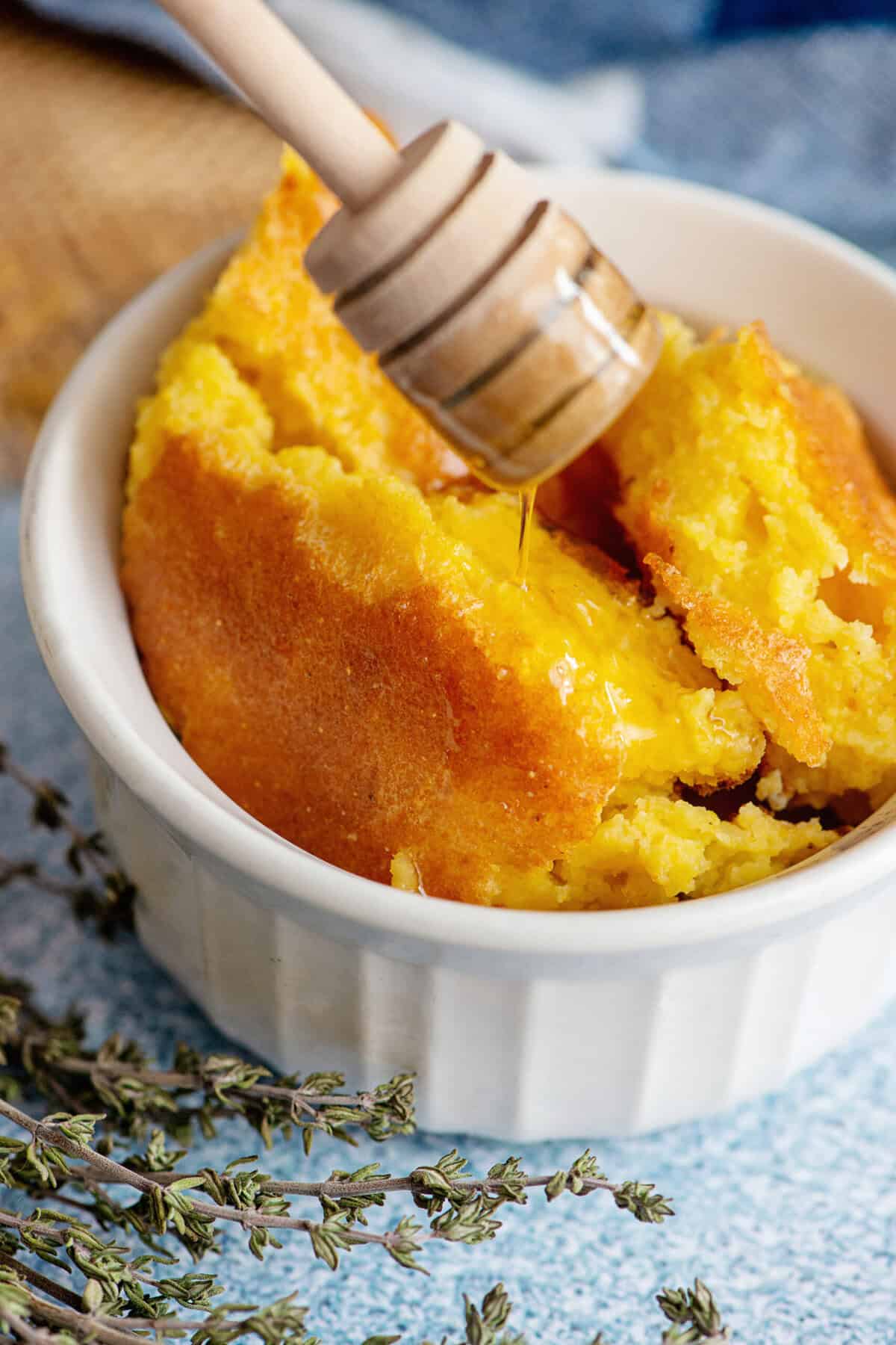 Close-up of Southern spoonbread in a baking dish drizzled with honey.