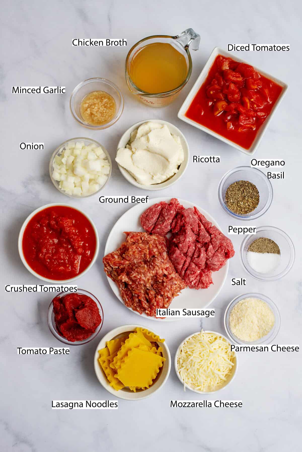 Ingredients for crockpot lasagna soup on a white marble surface.