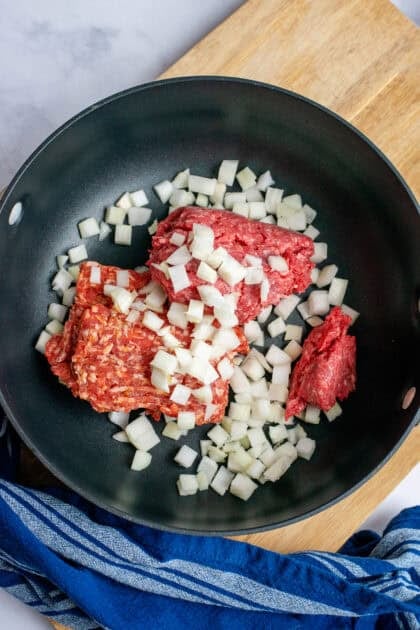 Adding beef and onions to a skillet for cooking.
