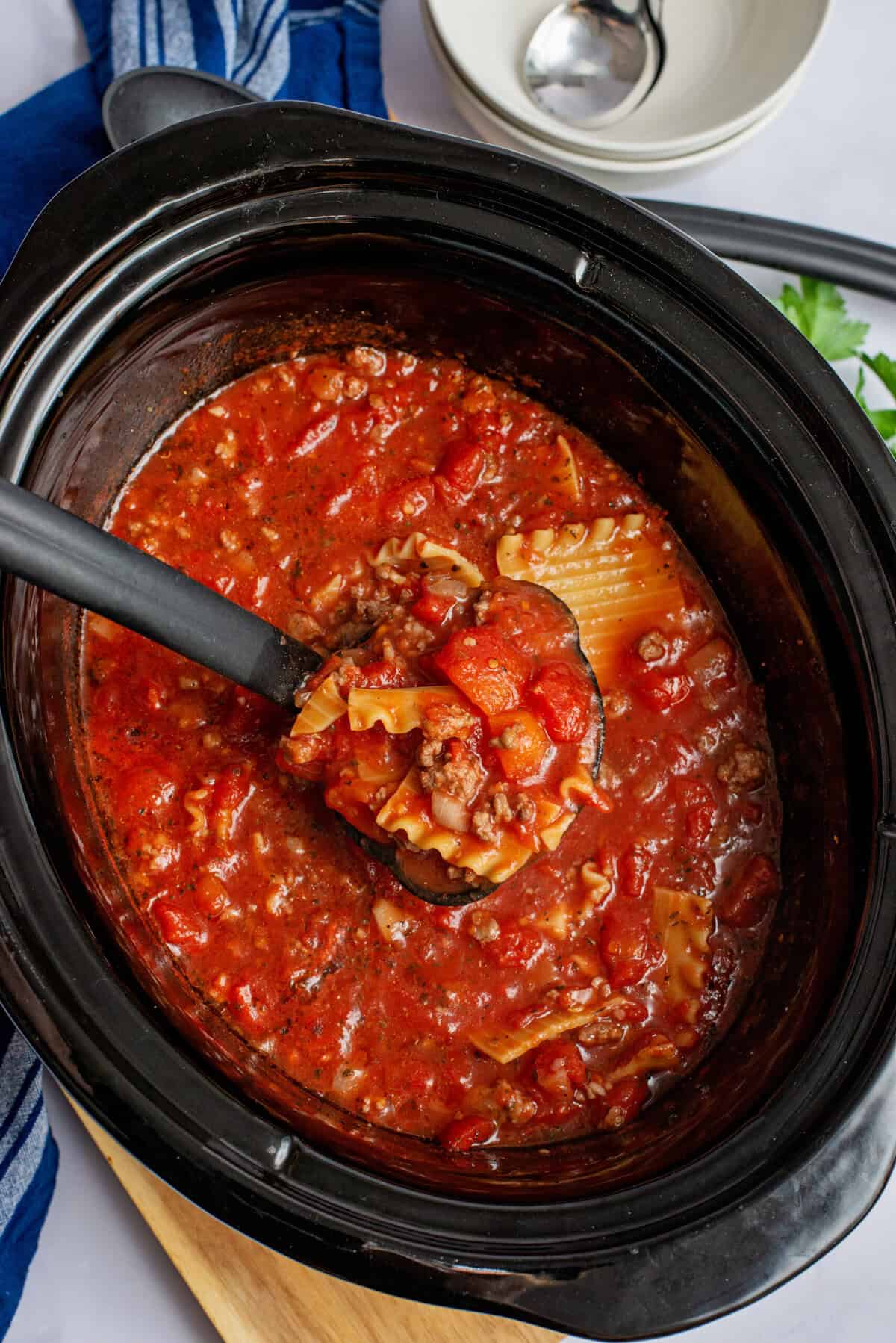 A ladle full of crockpot lasagna soup hovering over a crockpot.