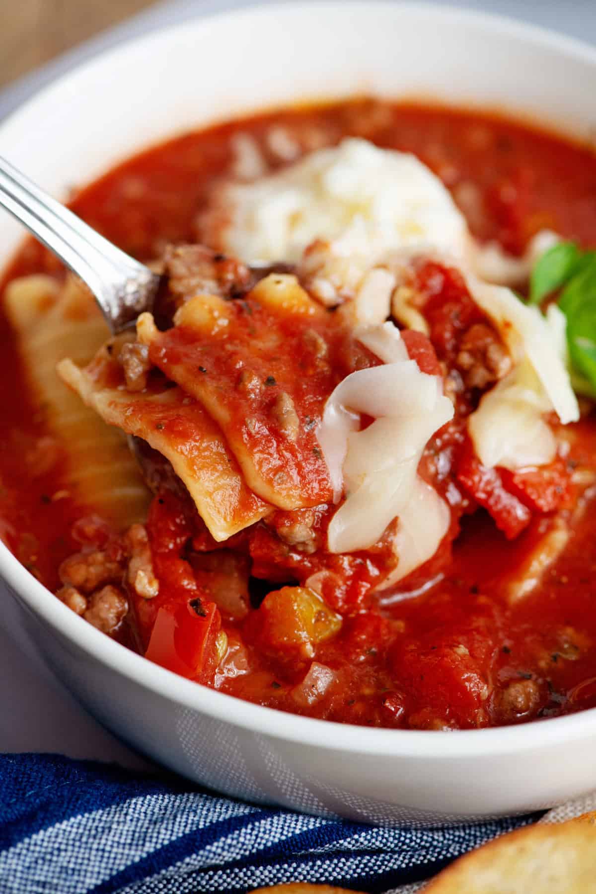 A spoonful of crockpot lasagna soup in a white bowl.