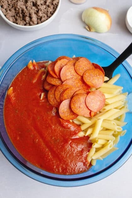 Pizza sauce, pepperoni, and pasta in a blue mixing bowl.