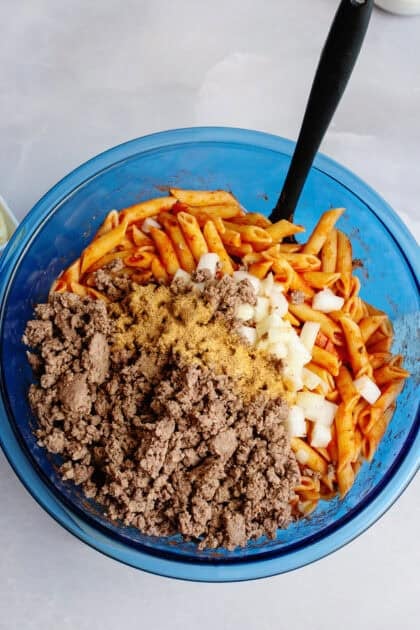 Ground beef, onions, and pasta in a blue mixing bowl.
