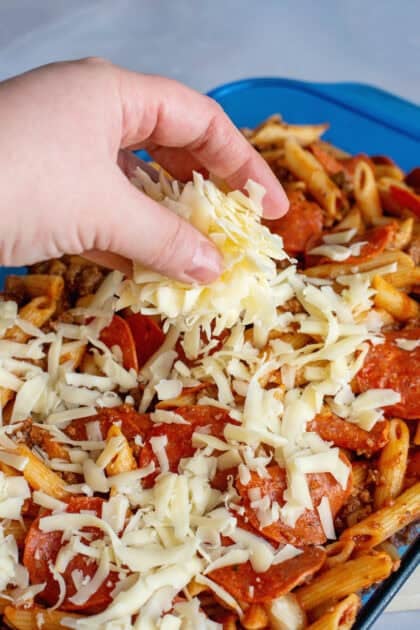 Adding shredded mozzarella cheese to pizza pasta casserole.