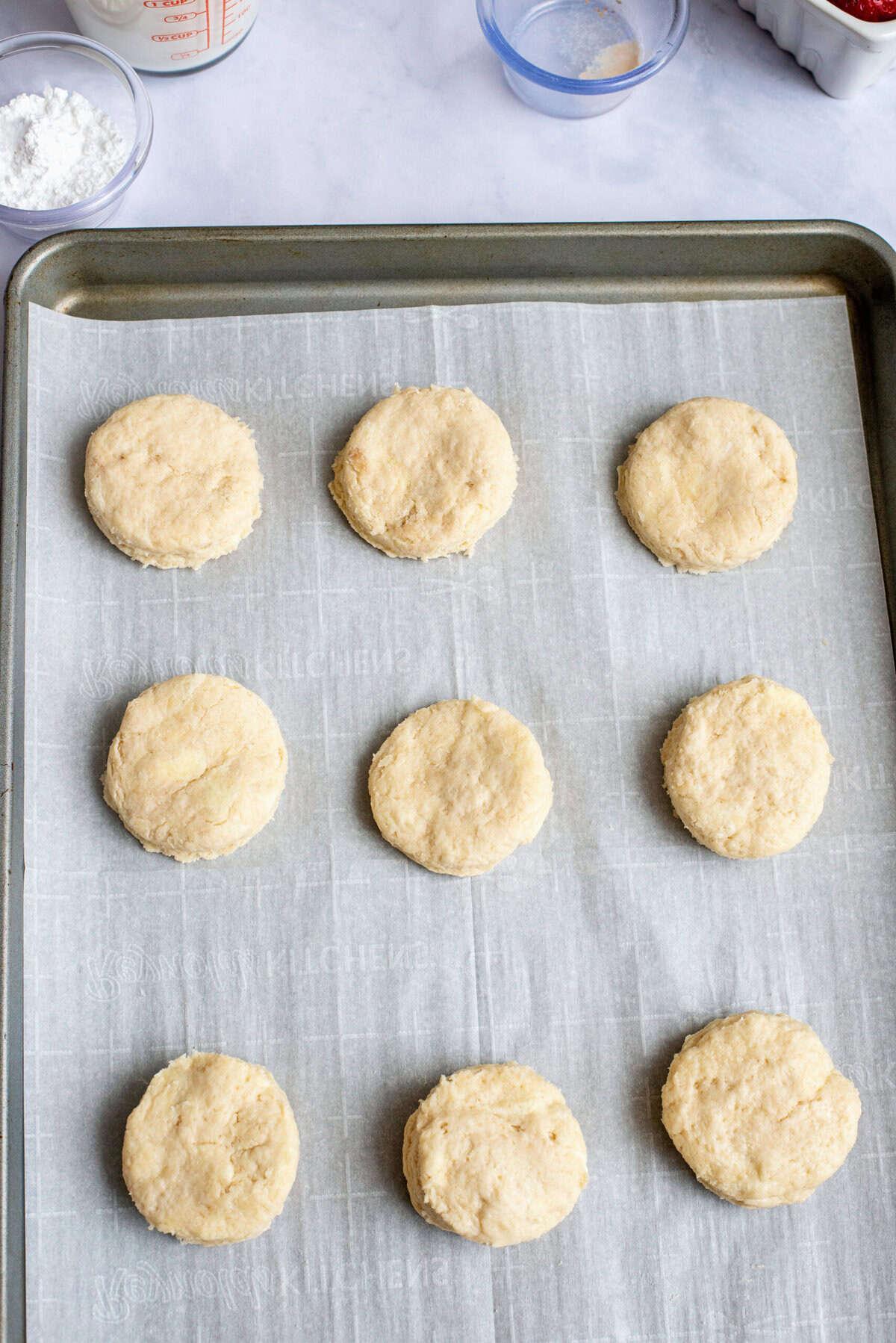 A row of biscuits on a baking sheet with parchment paper before going in the oven.