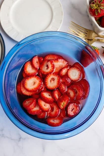 Sliced strawberries in a blue bowl soaked in sugar.
