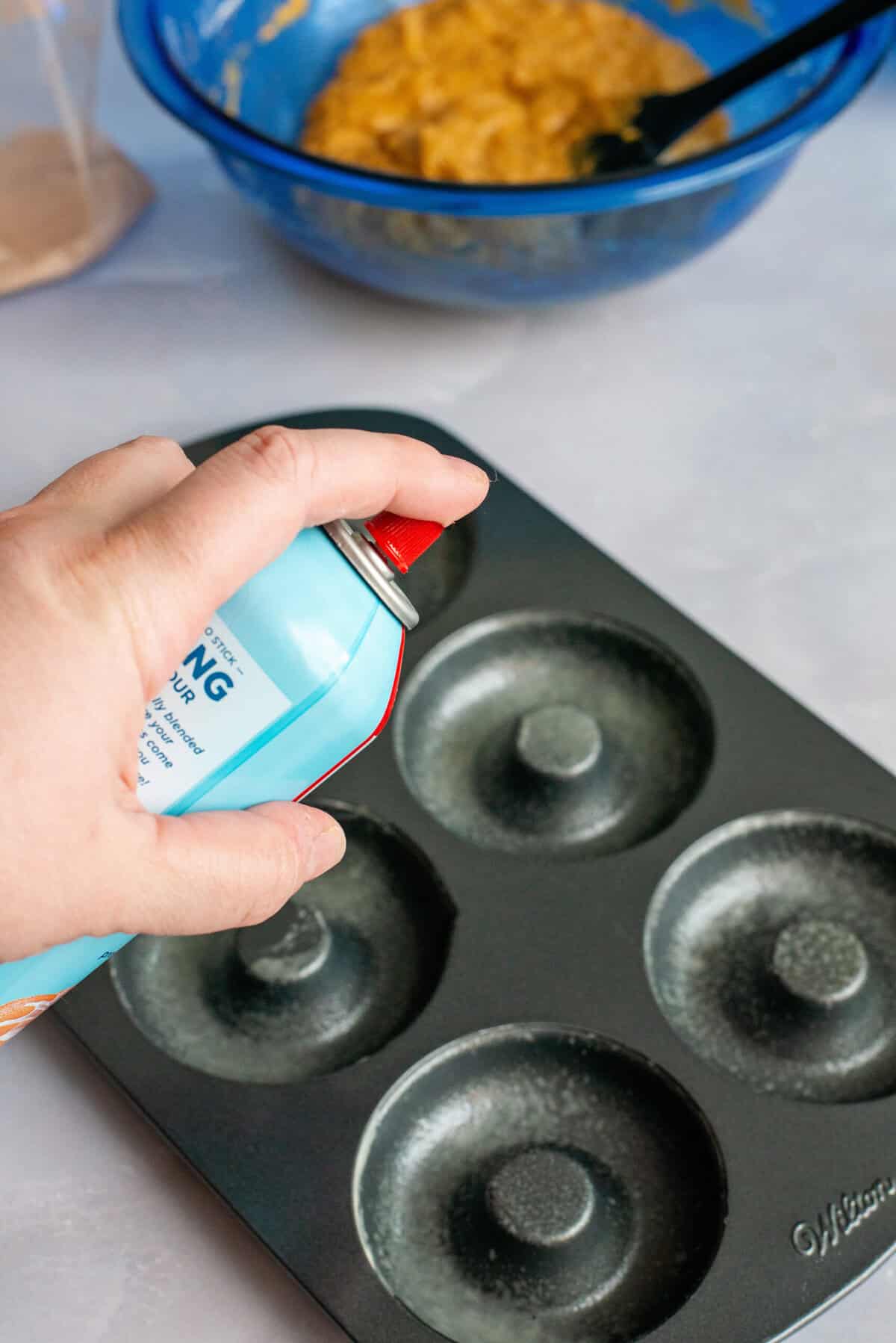 Spraying a donut pan with non-stick cooking spray.