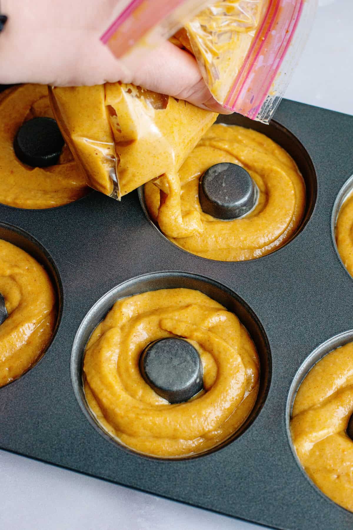 Piping donut batter into a donut tin.