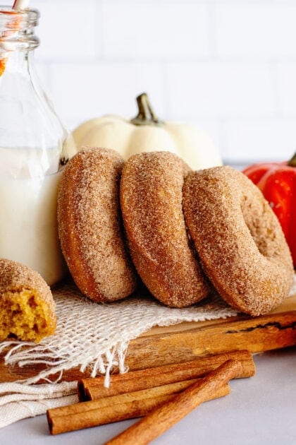 Pumpkin spice cake donuts in a row leaning on a glass jug of milk.