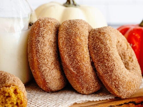 Pumpkin spice cake donuts in a row leaning on a glass jug of milk.