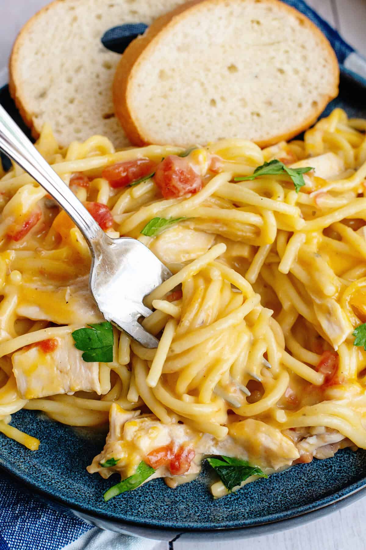 Fork twirling chicken spaghetti with bread on the side.
